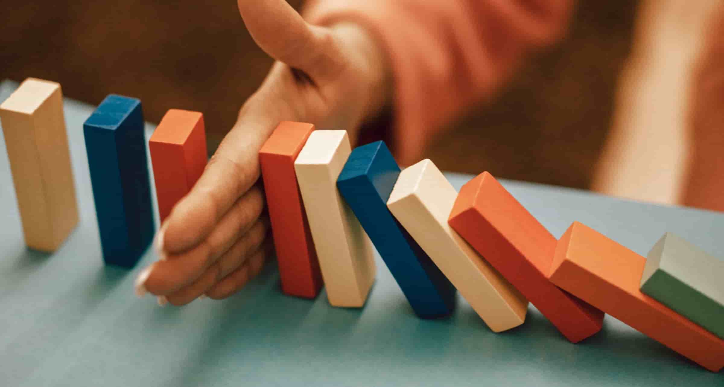 A hand protecting a line of falling wooden blocks.